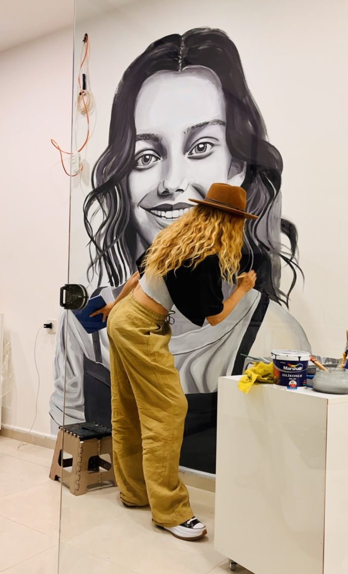 artist painting a portrait of a young Gil on an indoor mural in Istanbul