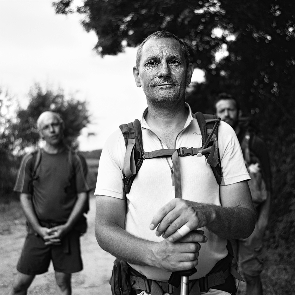 “Black and white portrait of a pilgrim on the Saint-Jacques-de-Compostelle, wearing a backpack, with nature visible in the background.”